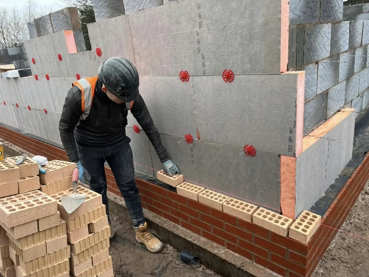 An RLG bricklayer laying facing bricks to the line on a new build, with the insulated blockwork inner leaf behind